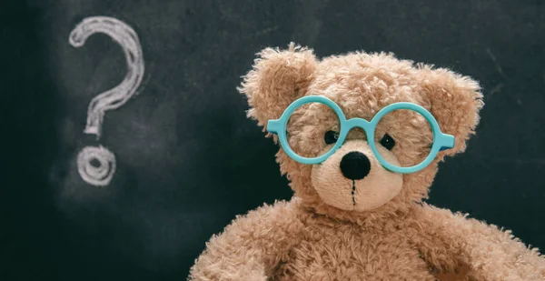 Roztomilý Teddy na brýlích s otazníkem na tabuli — Stock fotografie