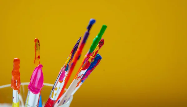 Paintbrushes with colorful paints on yellow color background, closeup view, copy space — Stock Photo, Image