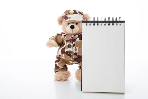 Schattige teddybeer in soldaat uniform en een blanco pad geïsoleerd tegen witte achtergrond — Stockfoto