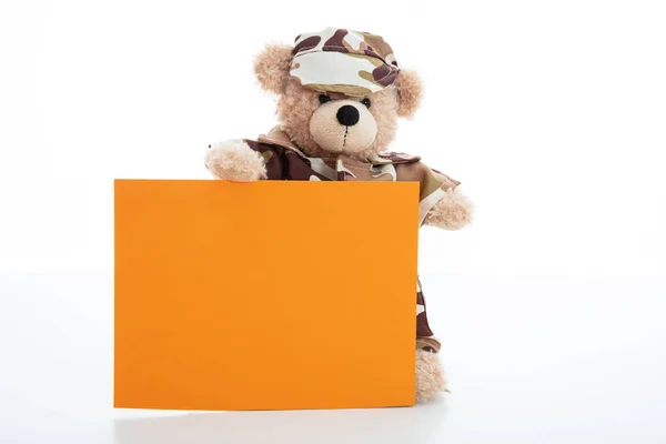 Cute teddy bear in soldier uniform and a blank orange color card isolated against white background — Stockfoto