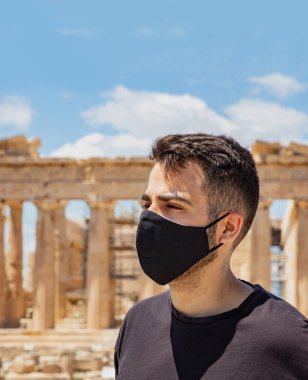 Atina Akropolü, Yunanistan koronavirüs günleri. Koruyucu yüz maskesi takan genç adam, Antik Yunan Partenon tapınağı ve mavi gökyüzü arka planı.