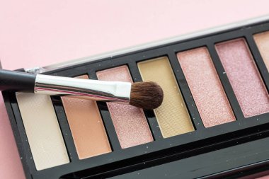 Göz farı paleti nötr renkler belirledi ve pembe arka plan üzerinde fırça, yakın görüş. Makyaj malzemeleri, güzellik salonu, kozmetik konsepti.