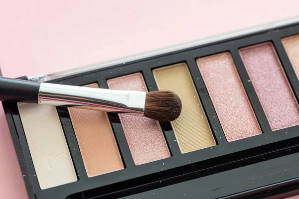 Eyeshadows pallete set neutral colors and brush against pink background, closeup view. Professional tools for make up, beauty salon, cosmetics concept