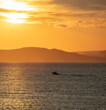 Deniz suyunun üzerinde gün batımı turuncu bulutlar. Ege Denizi Yunanistan 'da dramatik büyülü gündoğumu deniz manzarası. Karanlık ada kara ufku, alacakaranlık, şafak arkaplanı.