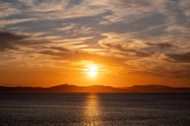 Deniz suyunun üzerinde gün batımı turuncu bulutlar. Ege Denizi Yunanistan 'da dramatik büyülü gündoğumu deniz manzarası. Karanlık ada kara ufku, alacakaranlık, şafak arkaplanı.