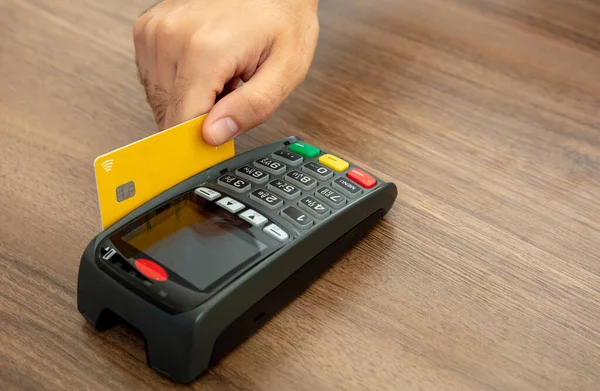 Hand swiping a credit card in a POS terminal on wood counter background, closeup view.Terminal cash register machine for cashless payment.