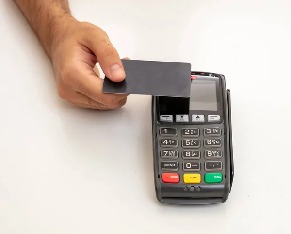 Payment with NFC technology. Hand holding a blank credit card over a POS terminal isolated on white background.Terminal cash register machine for contactless payment.