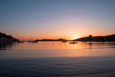 Kea Adası, Yunanistan. Deniz suyunda gün batımı turuncu rengi. Vourkari limanında demirli tekneler, dalgalı sularda altın yansımalar, Ege Akdeniz.