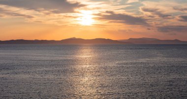 Deniz suyunun üzerinde gün batımı turuncu bulutlar. Ege Denizi Yunanistan 'da dramatik büyülü gündoğumu deniz manzarası. Karanlık ada kara ufku, alacakaranlık, şafak arkaplanı.