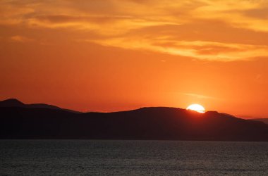 Deniz suyunun üzerinde gün batımı turuncu bulutlar. Ege Denizi Yunanistan 'da dramatik büyülü gündoğumu deniz manzarası. Alacakaranlık, şafak vakti. Kara ada ve turuncu bulutlu gökyüzü