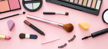 Makyaj malzemesi yatıyordu. Ruj ve tırnak cilası, göz farı ve allık, fırçalar ve kalemler pembe renk arka planına karşı, afiş