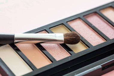 Göz farı renkleri ve pembe arka planda fırça, yakın görüş. Makyaj malzemeleri, güzellik salonu, kozmetik konsepti.