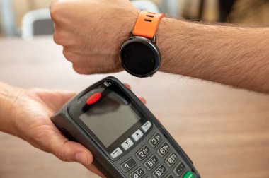 Mobil ödeme, akıllı saat NFC, saha iletişimi kablosuz teknolojisi. POS makinesi ve akıllı saat ile kasiyer ve müşteri elleri, yakın görünüm