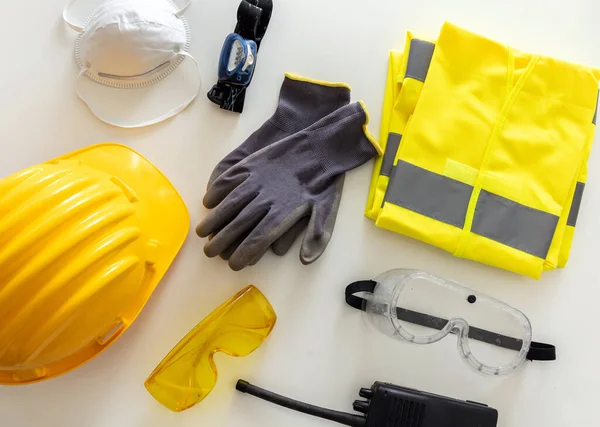 Work safety protection flat lay. Industrial protective gear reflective, fluorescent yellow color on white background, top view. Construction site health and safety equipment
