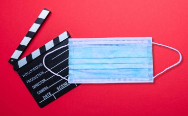 Sinema salonunda Coronavirus koruması. Tıbbi koruyucu yüz maskesi ve kırmızı arka planda film klasörü. COVID-19 hastalığın yayılmasını önleme