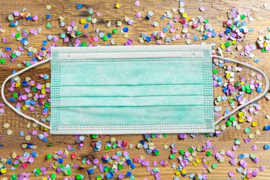 Karnaval 2020 partisi, koronavirüs günleri, koruyucu yüz maskesi, renkli konfeti ve tahta arka planda yılanlar. COVID 19 yayılma önleme önlemi