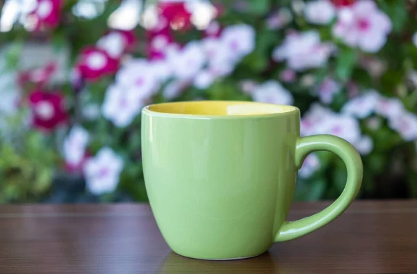 コーヒーカップは庭のテーブルの上でモックアップ 熱い飲み物のためのハンドルを持つ緑の色の空白のマグカップは 花の背景をぼかす ブランディングテンプレート — ストック写真