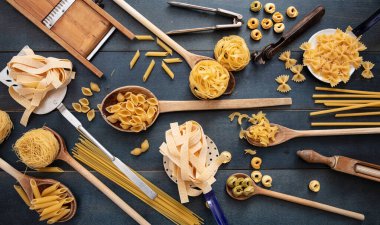 Makarna pişirme konsepti. Çiğ makarna çeşitli şekillerde ve klasik mutfak ekipmanları düz uzanır mavi ahşap masa arka planı, üst görünüm