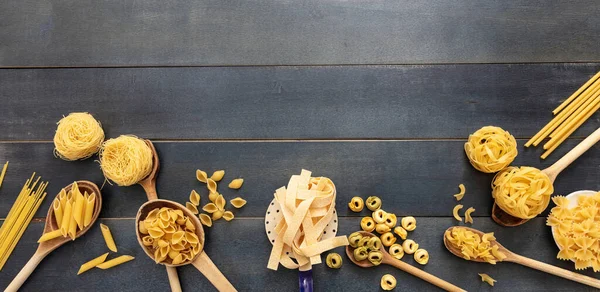 Pasta cooking concept. Raw pasta various shapes and spoons on blue wooden table background, top view