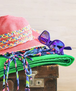 Beyaz arka planda yaz ve tatil aksesuarları. Turizm için yaz seyahati esasları, mayo, havlu, gözlük, eski bir bavula hasır şapka. Dikey fotoğraf. Kopyalama alanı.