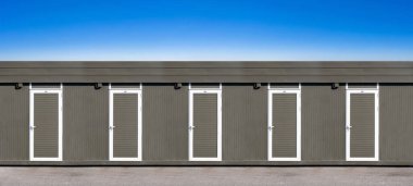 Kapıları umumi tuvaletlere ya da şantiye ofislerine çevrilmiş nakliye konteynırları, mavi gökyüzü geçmişi