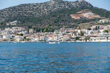 Denizden görünen Tolo Yunanistan kıyı manzarası. Yeşil tepeler, kayalık sahil şeridi ve sahil kasabası. Sakin mavi su ve berrak yaz gökyüzü,