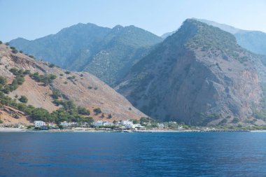Yunanistan 'ın Girit adasının güneybatı kıyısında sarp engebeli dağların eteğindeki Agia Roumeli köyü. Köye yaklaşan teknenin görüntüsü.