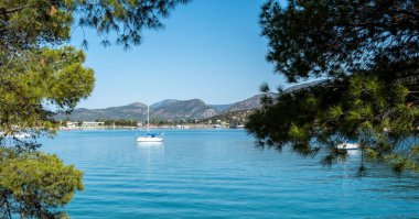 Ermioni Yunanistan 'ın sakin mavi suları, demirlemiş yelkenlileri, yamaçlardaki evleri ve açık yaz gökyüzüyle kıyı manzarası