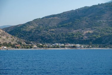 Yunanistan 'ın güneyindeki Girit adasındaki Sougia kıyı köyü. Öndeki mavi deniz ve arkadaki engebeli yeşil dağlar, mavi gökyüzü.