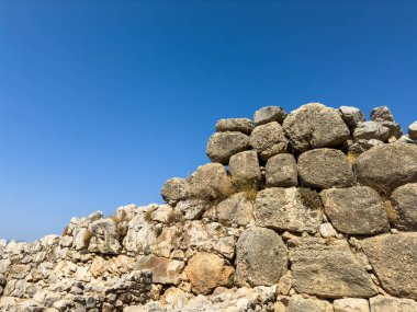 Yunanistan 'ın Mycenae kentindeki antik taş takviye duvarı, açık mavi yaz gökyüzü altında, alçak perspektiften parlak gün ışığında aşınan devasa bloklar