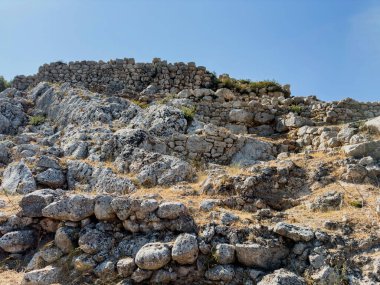 Yunanistan 'daki Miken arkeoloji sahasında yıpranmış taş duvarlar, açık yaz güneşi, açık mavi gökyüzü ve engebeli kayalık arazi