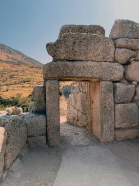 Yunanistan 'daki Mycenae arkeoloji sahasının tarihi taş geçidi, arka planda tepeler ile yaz güneşinin altında devasa yıpranmış bloklar.