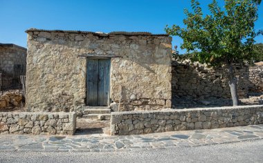 Kırsal mavi ahşap kapılı ve metal çatılı yıpranmış taş ev, Yunanistan 'ın Gavdos adasındaki Kastri köyünde küçük bir ağaç..