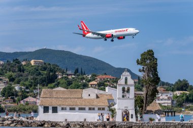 Korfu, Yunanistan, 5 Haziran 2025. Corendon Havayolları 'nın ticari uçağı, güneşli bir günde tarihi Vlacherna Manastırı' na doğru alçalıyordu.