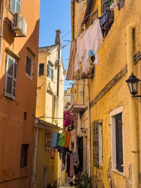 Yunanistan 'ın eski Corfu kasabasının dar sokağında çamaşırhane var. Çiçekli begonviller ve geleneksel binalar. Akdeniz sokak manzarası.