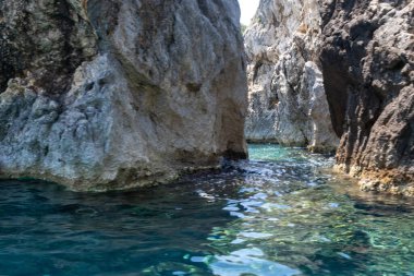 Berrak turkuvaz denizinden yükselen sarp kayalıklar, dalgalanan sulara yansıyan güneş ışığı, Korfu adası Yunanistan, Paleokastritsa