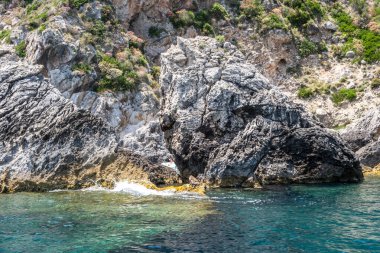 Berrak turkuvaz denizinden yükselen sarp kayalıklar, dalgalanan sulara yansıyan güneş ışığı, Korfu adası Yunanistan, Paleokastritsa