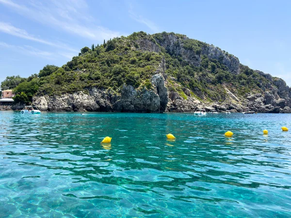 Korfu, Yunanistan 'da turkuaz deniz suyuyla kayalık kıyı şeridi. Güneşli bir yaz günü, berrak gökyüzü, yemyeşil ve sudaki sakin yansımalar
