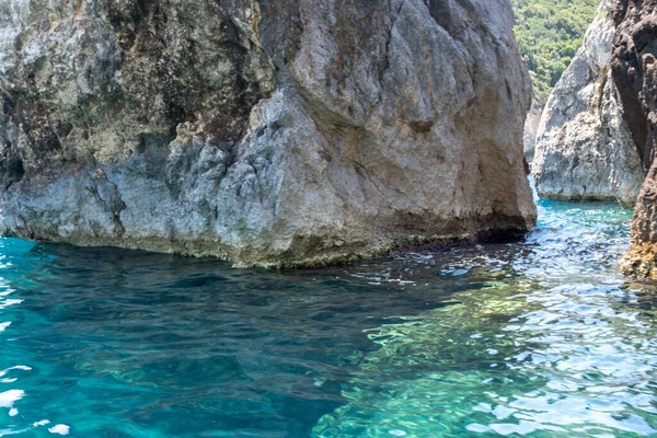 Berrak turkuaz denizden yükselen sarp kayalıklar, dalgalı sulara yansıyan güneş ışığı, yemyeşil alanlar, Korfu adası Yunanistan