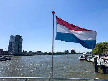 Rotterdam şehri modern mimari kuleleri ve Hollanda bayrağı dalgalanması, mavi gökyüzü. Hollanda