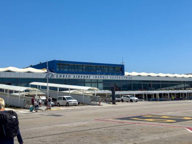 Korfu, Yunanistan, 4 Haziran 2025. Bagajlı gezginler pisti aşarak uluslararası Corfu Ioannis Kapodistrias Havaalanı terminaline doğru yürüyorlar.