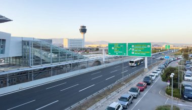 Atina, Yunanistan, 8 Mayıs 2025. Park halindeki arabaların, geçen otobüslerin ve kontrol kulesinin bulunduğu işlek havaalanı yolu, temiz bir gökyüzü.