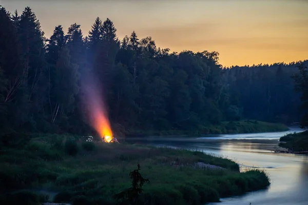 Bonfire on the river bank near the forest. Twilight.