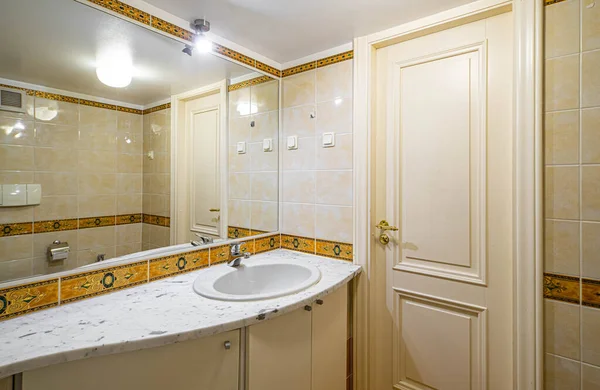 Modern interior of small bathroom with brown tile. Sink and closed door.