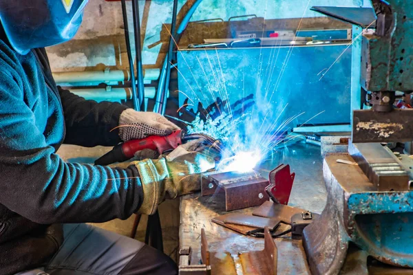 Worker in welding mask at factory. Welding process. Electric welding. Bright yellow sparks.