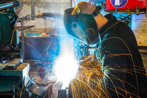 Worker in welding mask at factory. Welding process. Electric welding. Bright yellow sparks.