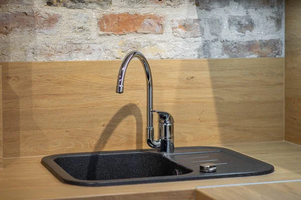 Black sink in modern loft kitchen. Wooden surface. Brick wall. Close-up.