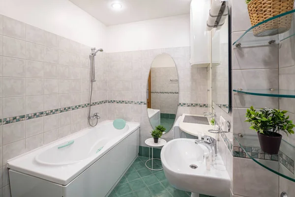 Light interior of modern spacious bathroom. White sink and mirror. Flowers on shelves. Large bath. Washing machine.