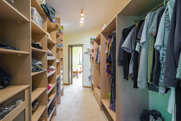 Modern interior of dressing room in luxury apartment. Full drawers and shelves. Big wardrobe with clothes.