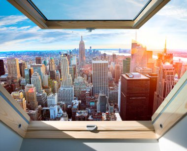 New York 'un ufuk çizgisinin nefes kesici görüntüsü modern bir gökdelenden çekiliyor. Batan güneş, ikonik binaların üzerine sıcak tonlar saçıyor. Bulutlarla benekli açık mavi gökyüzünün altındaki hareketli metropolü aydınlatıyor..